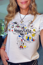 Load image into Gallery viewer, A woman wearing a white graphic t-shirt featuring a colorful map of Venezuela with the word 'VENEZUELA' printed across the chest, shown in a selfie-style indoor photo.
