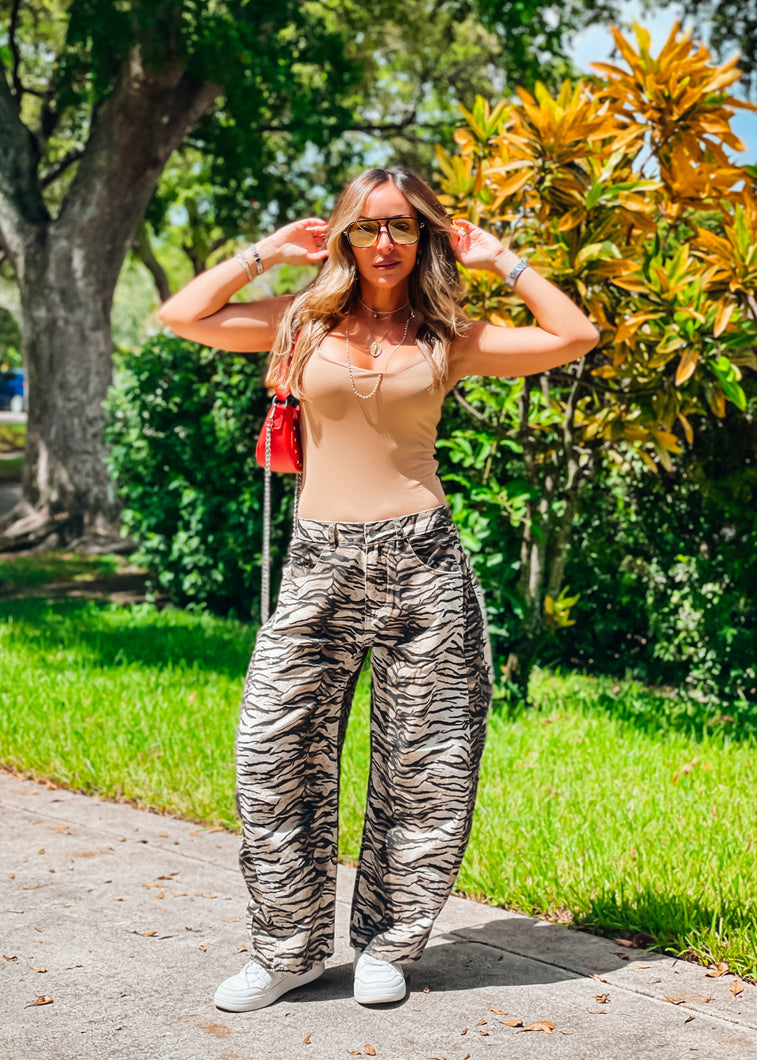 Woman in zebra print pants and red top standing outdoors with greenery in the background